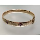 A diamond and ruby-set 9ct gold bangle, the hinged bangle set to one half with three flowerhead