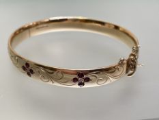 A diamond and ruby-set 9ct gold bangle, the hinged bangle set to one half with three flowerhead