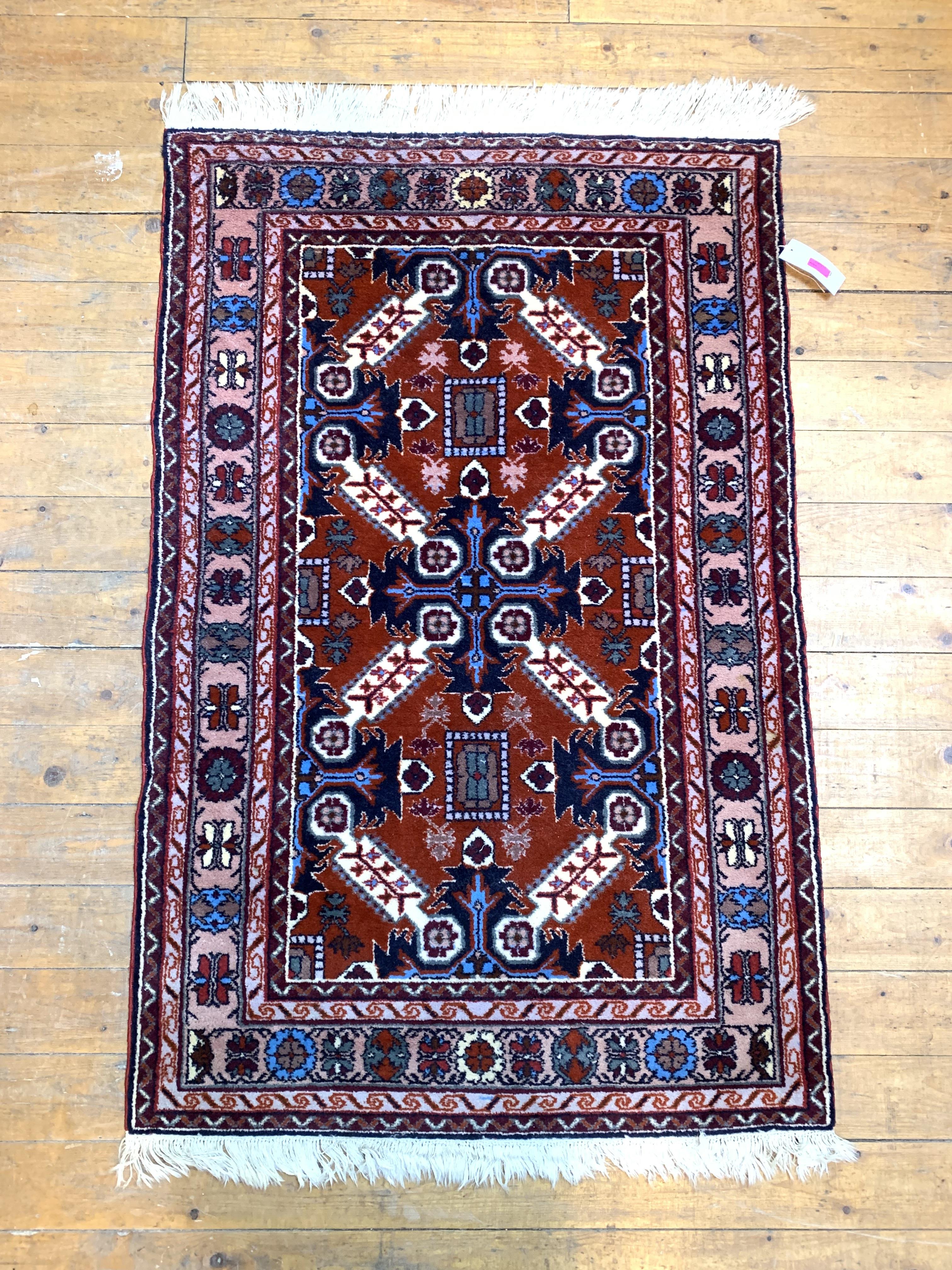 A hand knotted North West Persian rug, the madder ground of repeating design enclosed by double