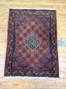 A hand knotted Persian Senneh design rug, with lozenge medallion on a busy red field and bordered,