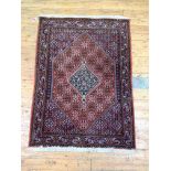 A hand knotted Persian Senneh design rug, with lozenge medallion on a busy red field and bordered,