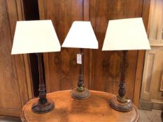 A group of three mahogany table lamps with tapering column style stems issuing from tulips on