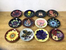 A group of twelve Moorcroft trinket dishes, each with different flower or plant, of various ages,