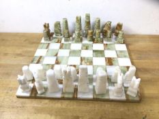 A polished and carved stone part chess set, lacking one pawn, board measures 36cm x 36cm