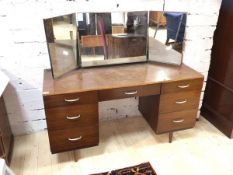 A mid century teak veneered dressing table with triple swing mirror over one long and six short