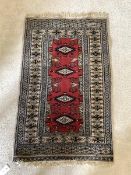 A small hand knotted Afghan rug, the red field with lozenge medallions and bordered 108cm x 63cm