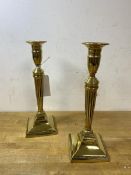 A pair of brass classically inspired candlesticks, each on a tapering column mounted on square base,