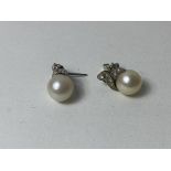 A pair of cultured pearl white metal mount milligrain set stud earrings with scrolling mount to top