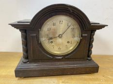 A 1920's oak mantel clock of architectural form, dial with arabic numerals, on bun feet, label to
