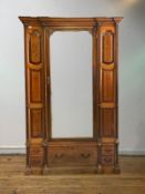 A late 19th/ early 20th century oak wardrobe of architectural form, the dentil cornice over a mirror