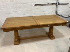 A large light oak extending dining table, the rectangular top with one additional leaf, raised on