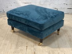 A contemporary footstool, upholstered in teal crushed velvet, raised on turned supports with brass