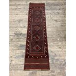 A Meshwani runner rug, the red ground with repeating lozenge medallions and bordered, 231cm x 54cm