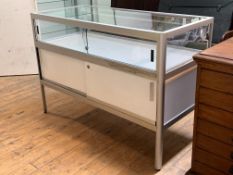 A modern glass and aluminum jewellery display cabinet, the top with two sliding doors over two