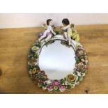 A Dresden china framed mirror, with two cherubs on floral encrusted frame, a crown above an s to