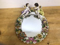 A Dresden china framed mirror, with two cherubs on floral encrusted frame, a crown above an s to