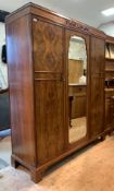 A figured walnut triple wardrobe, the frieze with scrolled acanthus decoration over an arched