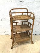 A cane and wicker open shelf with three tiers on splayed supports (89cm x 50cm x 37cm)