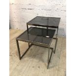 A nesting pair of contemporary side tables with smoked glass in polished metal frames, (larger