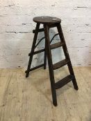 A first half 20thc elm folding step ladder with circular top with pierced handle over three
