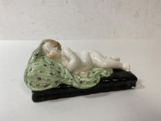 An early 19thc figure of young child asleep on blankets, (5cm h x 12cm x 6cm)