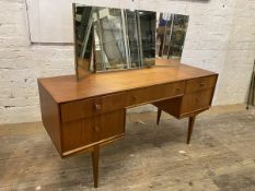 A mid century teak dressing table with tryptic mirror over rectangular top, base having