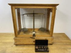 An early 20thc set of scales in wooden and glazed showcase, with fitted drawer to base, back foot