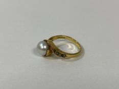 An 18 ct gold pearl and demantoid garnet ring, circa 1900, the central pearl in cross over