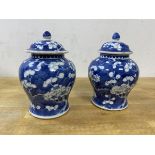 A pair of Chinese porcelain blue and white lidded baluster shaped jars with prunus decoration, chips