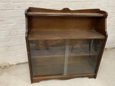 A waterfall bookcase with moulded top above single shelf, base with two sliding glass doors before