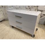 A contemporary white laminate chest fitted with three drawers raised on castors,