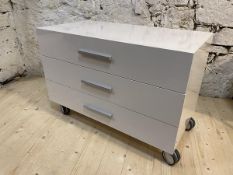 A contemporary white laminate chest fitted with three drawers raised on castors,