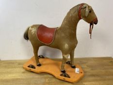 A vintage child's toy horse with horse hair exterior and leather saddle on wooden base with four