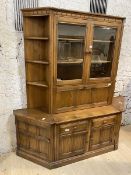 An Ercol elm dresser with two glazed doors with plate rails to interior over fall front door, having