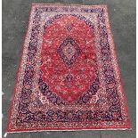 A Persian Kashan design handknotted rug, red field with blue medallions and spandrels, trailing