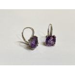 A pair of amethyst and diamond earrings, each with a cushion cut amethyst claw set beneath a line of