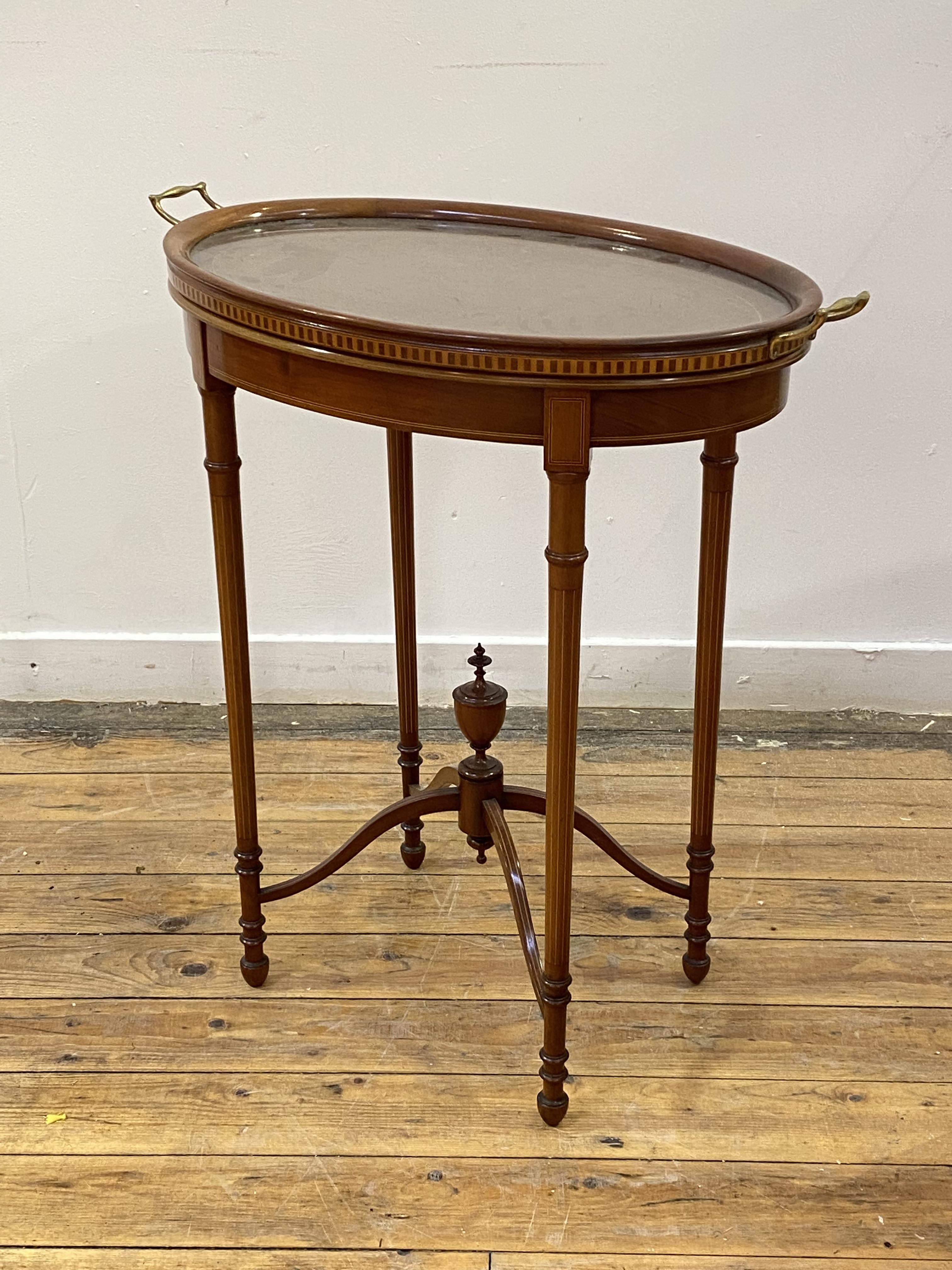 An Edwardian mahogany occasional table of oval outline, the lift off tray top with twin gilt brass