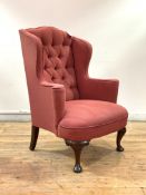 A George III style mahogany wingback armchair, 19th century, upholstered in deep buttoned faded