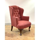 A George III style mahogany wingback armchair, 19th century, upholstered in deep buttoned faded