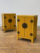 A pair of Chinese yellow lacquered bedside cabinets, each with two panelled doors enclosing shelf,