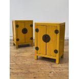 A pair of Chinese yellow lacquered bedside cabinets, each with two panelled doors enclosing shelf,