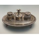 An early 19th century silver desk standish, the oval stand with gadrooned edge and raised on