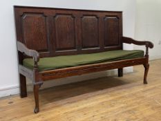 An 18th century vernacular oak settle, the four panel back above scrolled open arms and squab