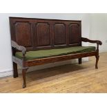 An 18th century vernacular oak settle, the four panel back above scrolled open arms and squab