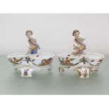 A pair of Berlin porcelain figural salts, each modelled with a putto and twin oval ozier-moulded