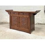 A Chinese hardwood alter table cabinet, the panelled top with scroll ends over two drawers and