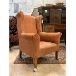 An Edwardian wingback armchair in the Georgian taste, upholstered, raised on square tapered supports