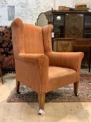An Edwardian wingback armchair in the Georgian taste, upholstered, raised on square tapered supports