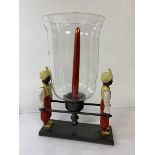 A cast painted metal candle centrepiece with candlestick and glass shade carried by two litter-