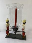 A cast painted metal candle centrepiece with candlestick and glass shade carried by two litter-